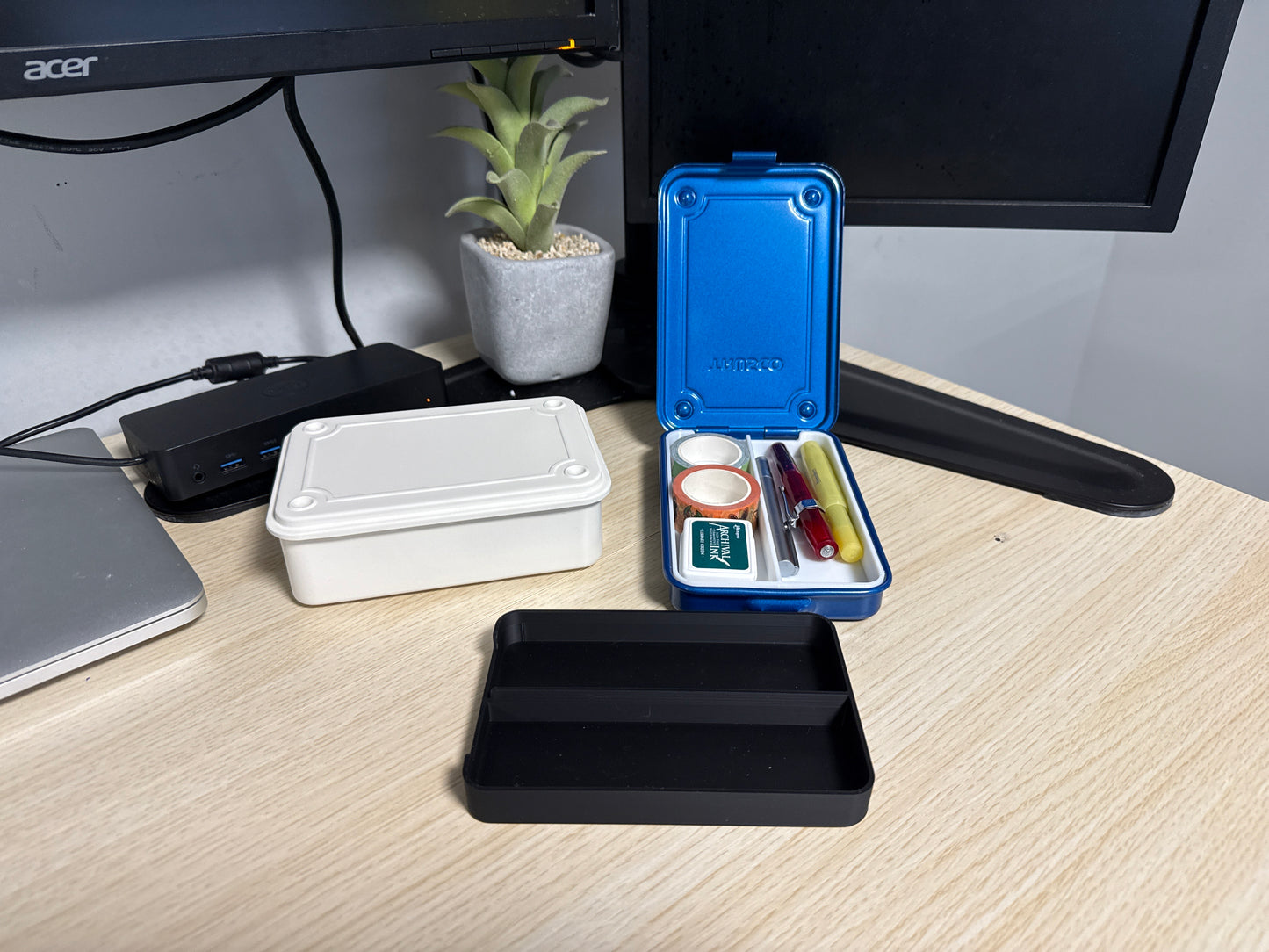 A set of 3D printed black inserts of various sizes displayed on a desk next to a blue trusco toolbox, and a silver trusco toolbox.