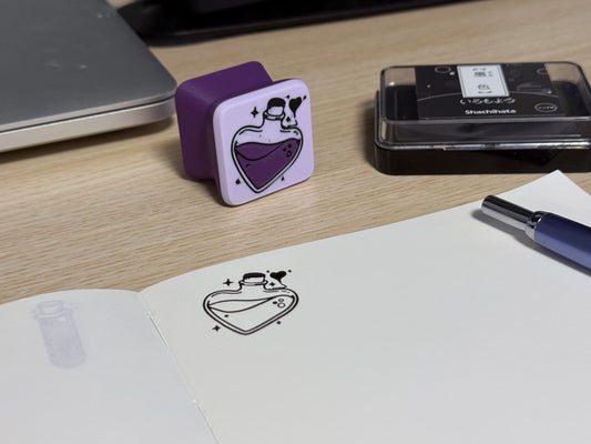 A customized heart-shaped ink stamp stamped on a book, placed on a desk next to a pen and a inkpad.