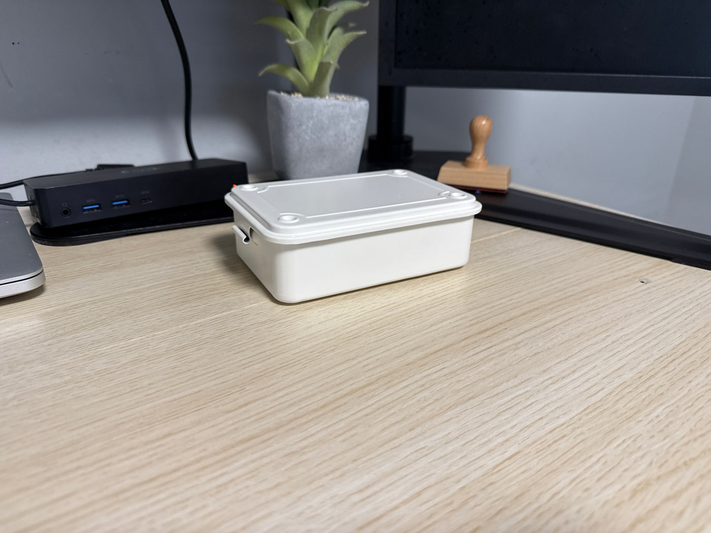 A white Toyo T-150 stackable tool box placed on a wooden surface, with a laptop, plant, and other items in the background.