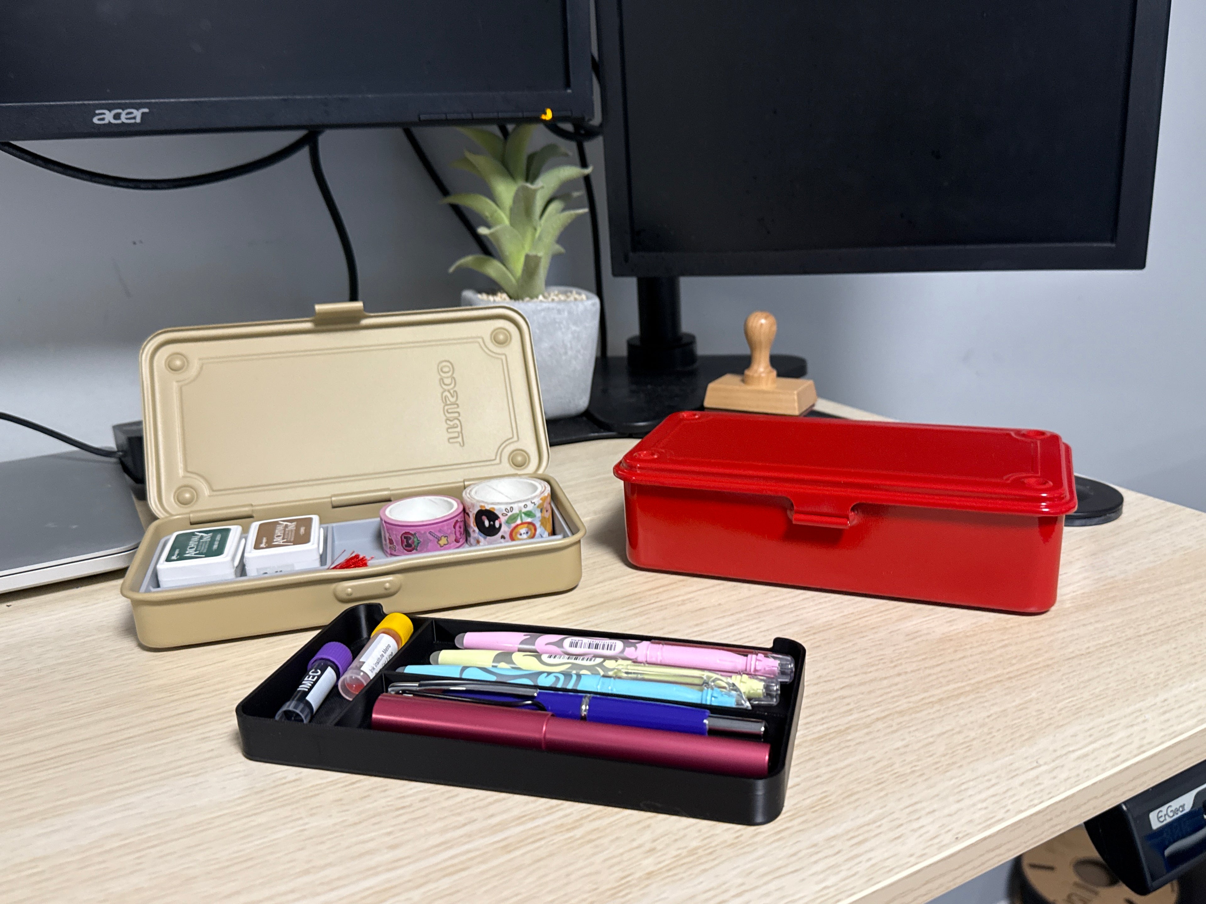 A set of 3D printed black inserts of various sizes displayed on a desk next to a beige toyo toolbox, and a red toyo toolbox. filled with washi tape and ink pads.