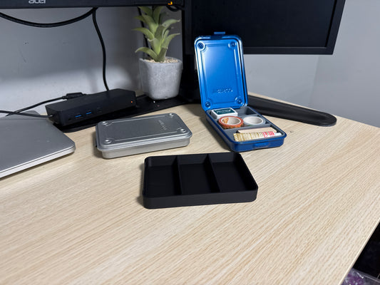 A set of 3D printed black inserts of various sizes displayed on a desk next to a blue trusco toolbox, and a silver trusco toolbox.