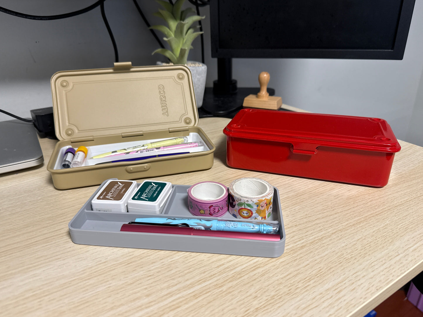 A set of 3D printed gray inserts of various sizes displayed on a desk next to a beige toyo toolbox, and a red toyo toolbox. filled with washi tape and ink pads.