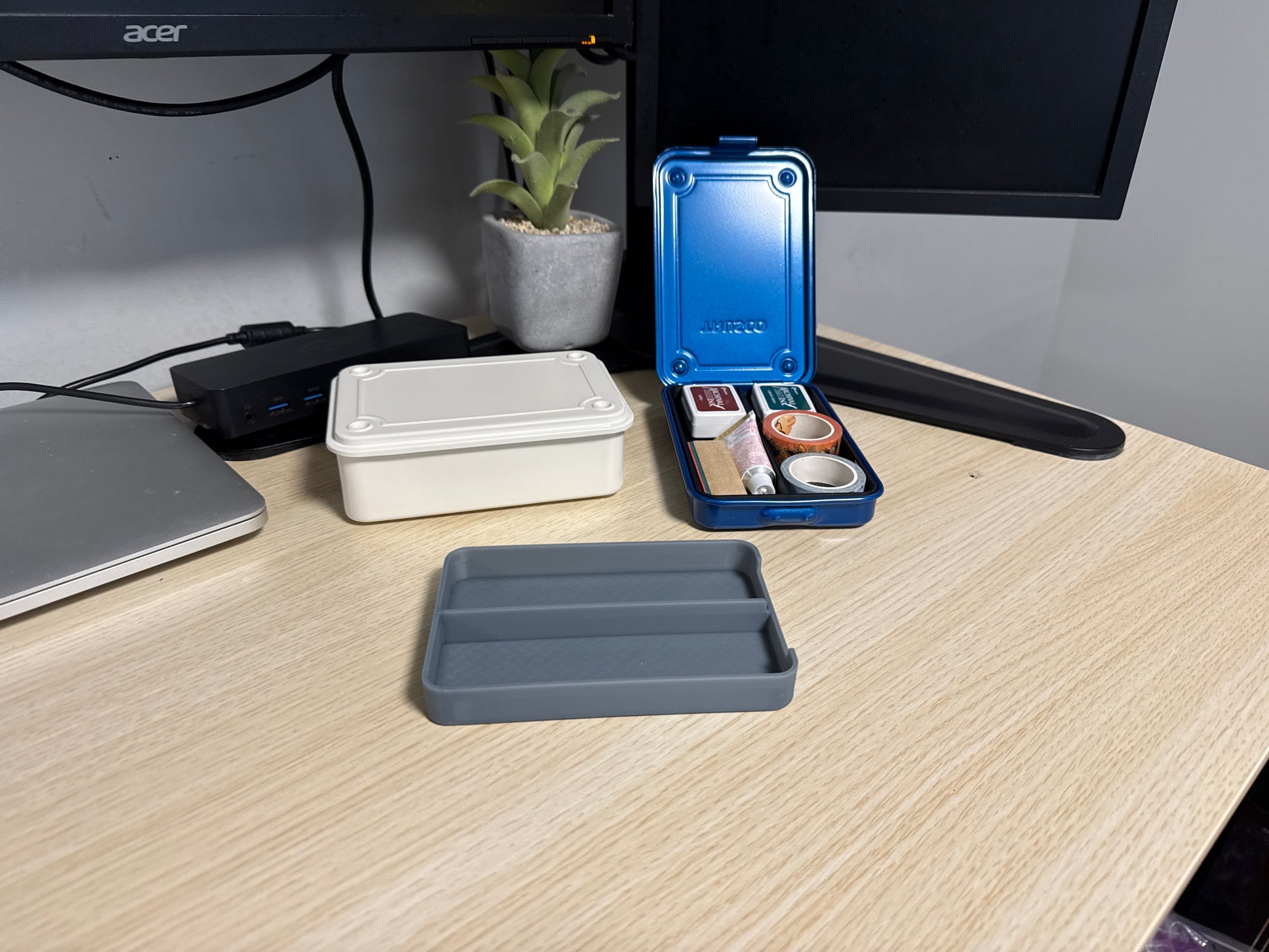 A set of 3D printed gray inserts of various sizes displayed on a desk next to a blue trusco toolbox, and a silver trusco toolbox.