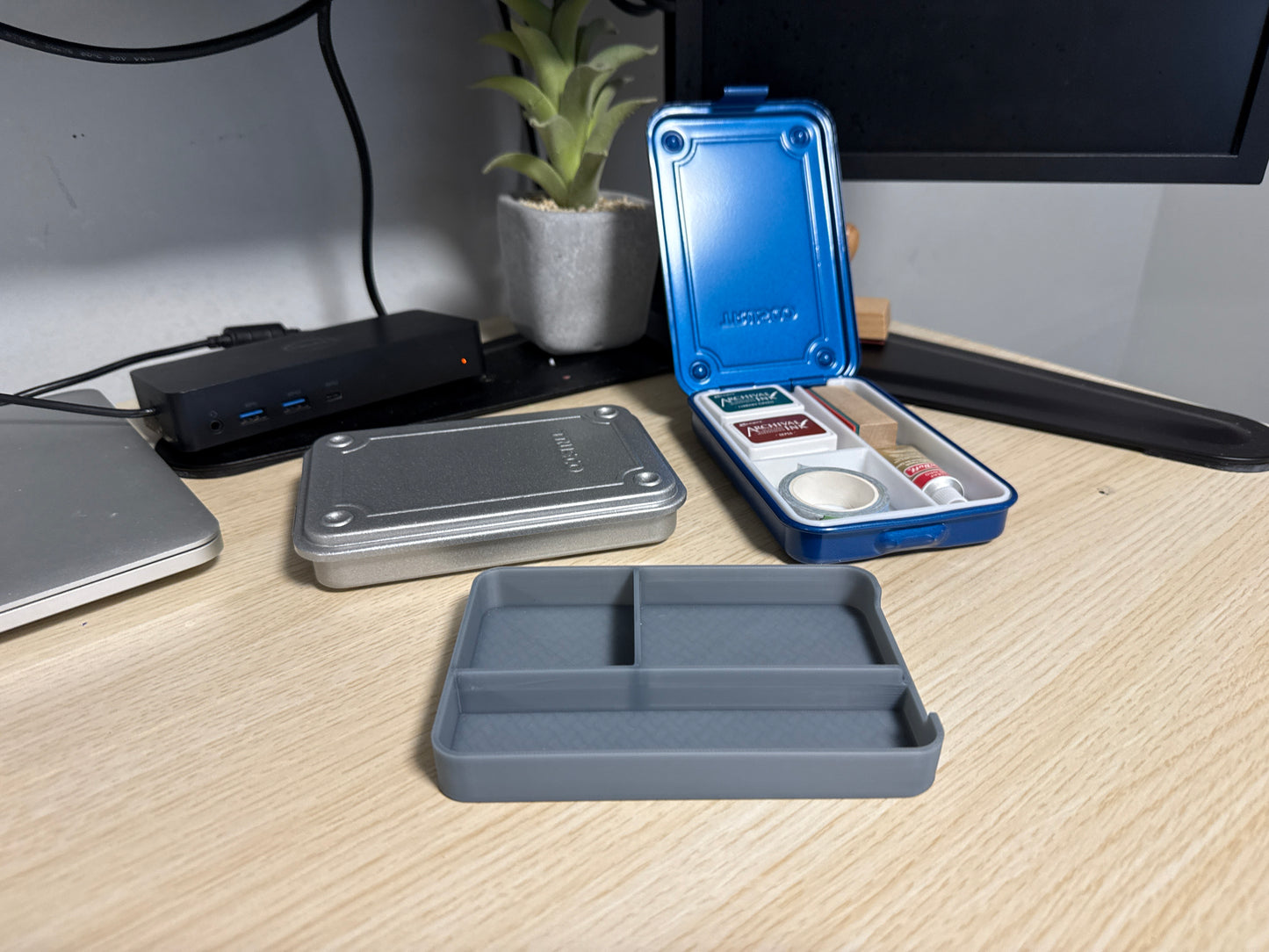 A set of 3D printed gray inserts of various sizes displayed on a desk next to a blue trusco toolbox, and a silver trusco toolbox.