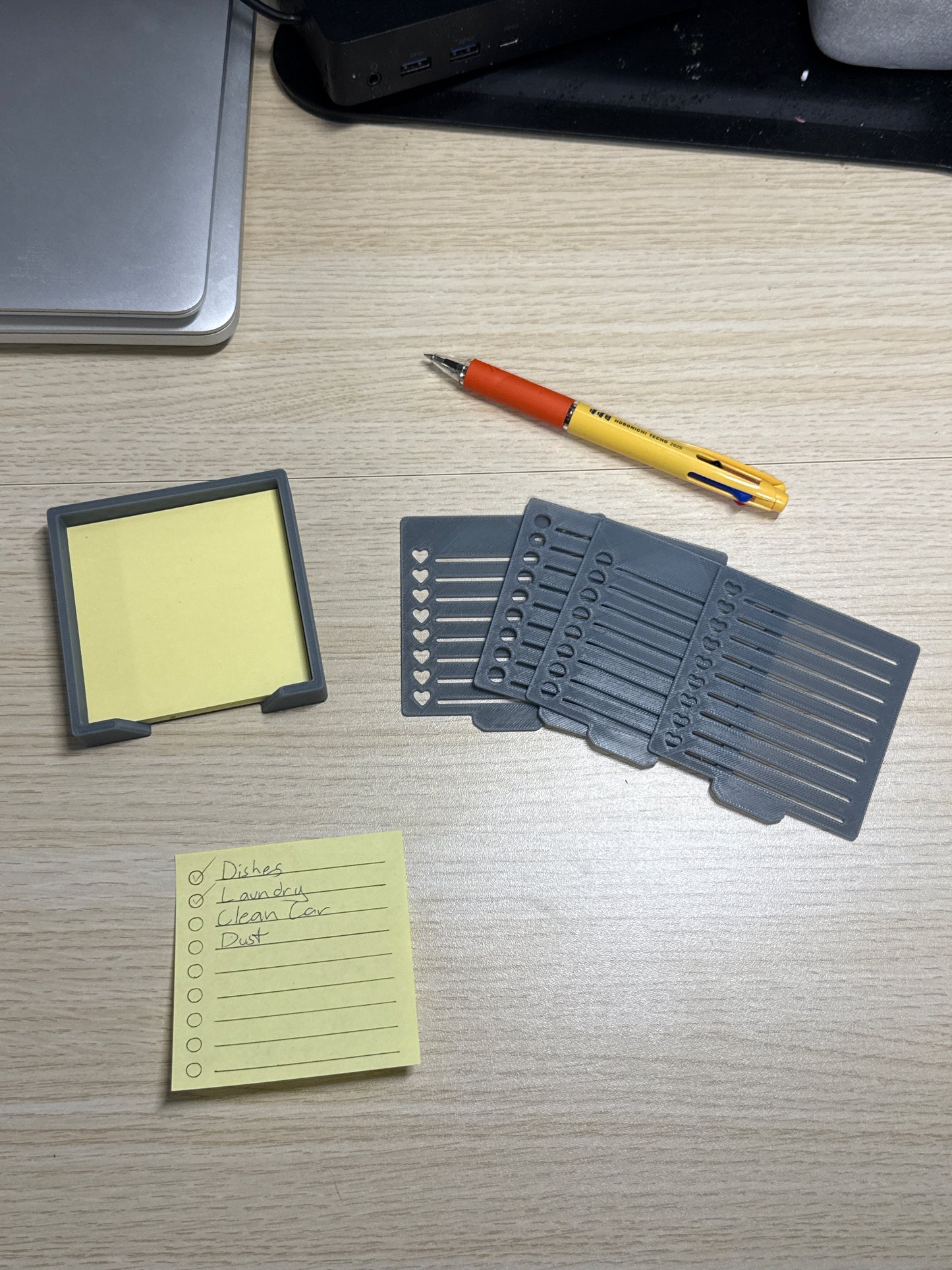 A collection of sticky notes, a pen, and a biodegradable plastic holder with stencils, displayed on a wooden desk.