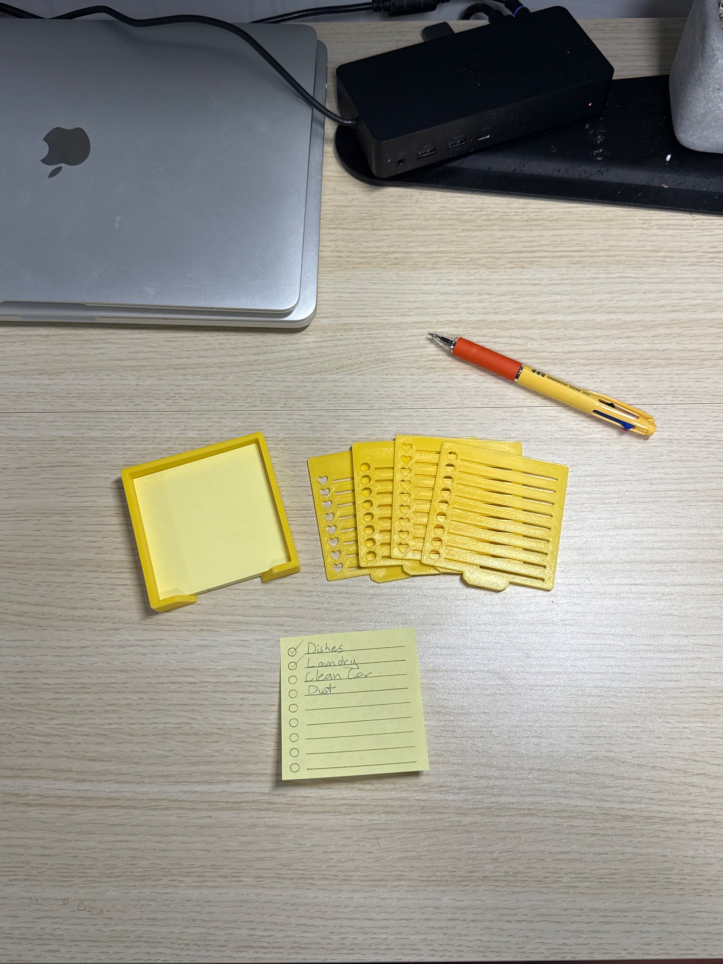 A collection of sticky notes, a pen, and a biodegradable plastic holder with stencils, displayed on a wooden surface.
