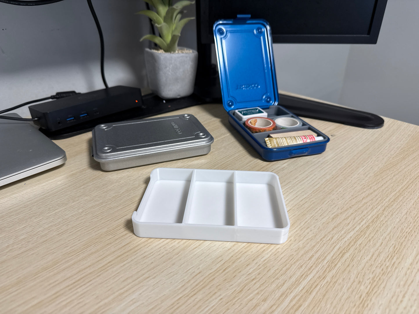 A set of 3D printed white inserts of various sizes displayed on a desk next to a blue trusco toolbox, and a silver trusco toolbox.