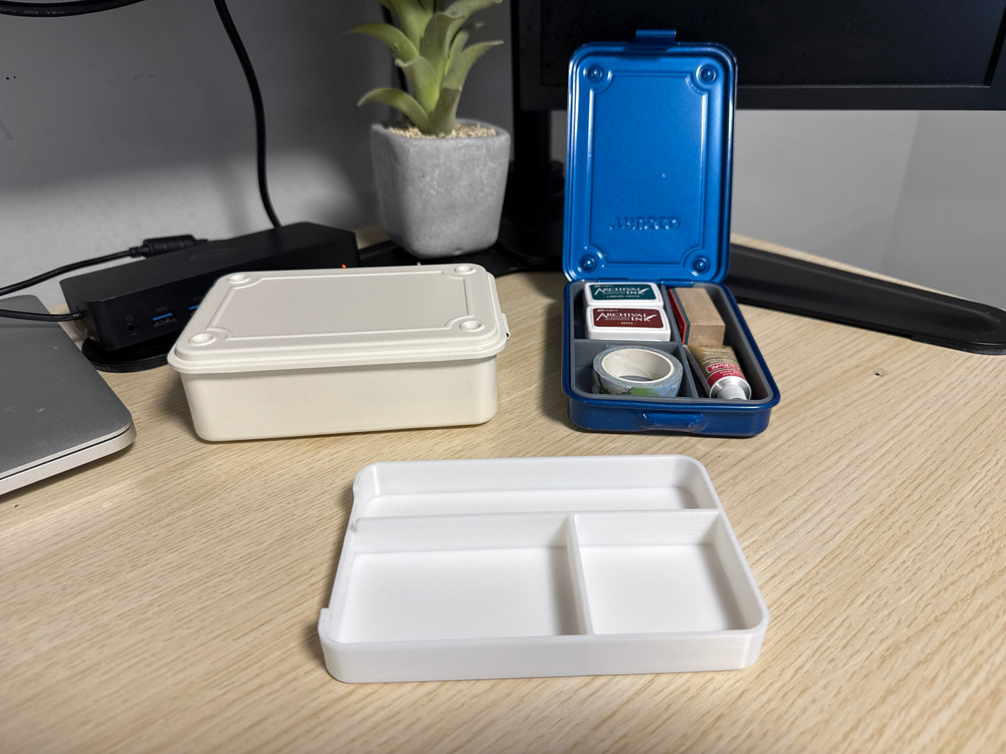 A set of 3D printed white inserts of various sizes displayed on a desk next to a blue trusco toolbox, and a silver trusco toolbox.