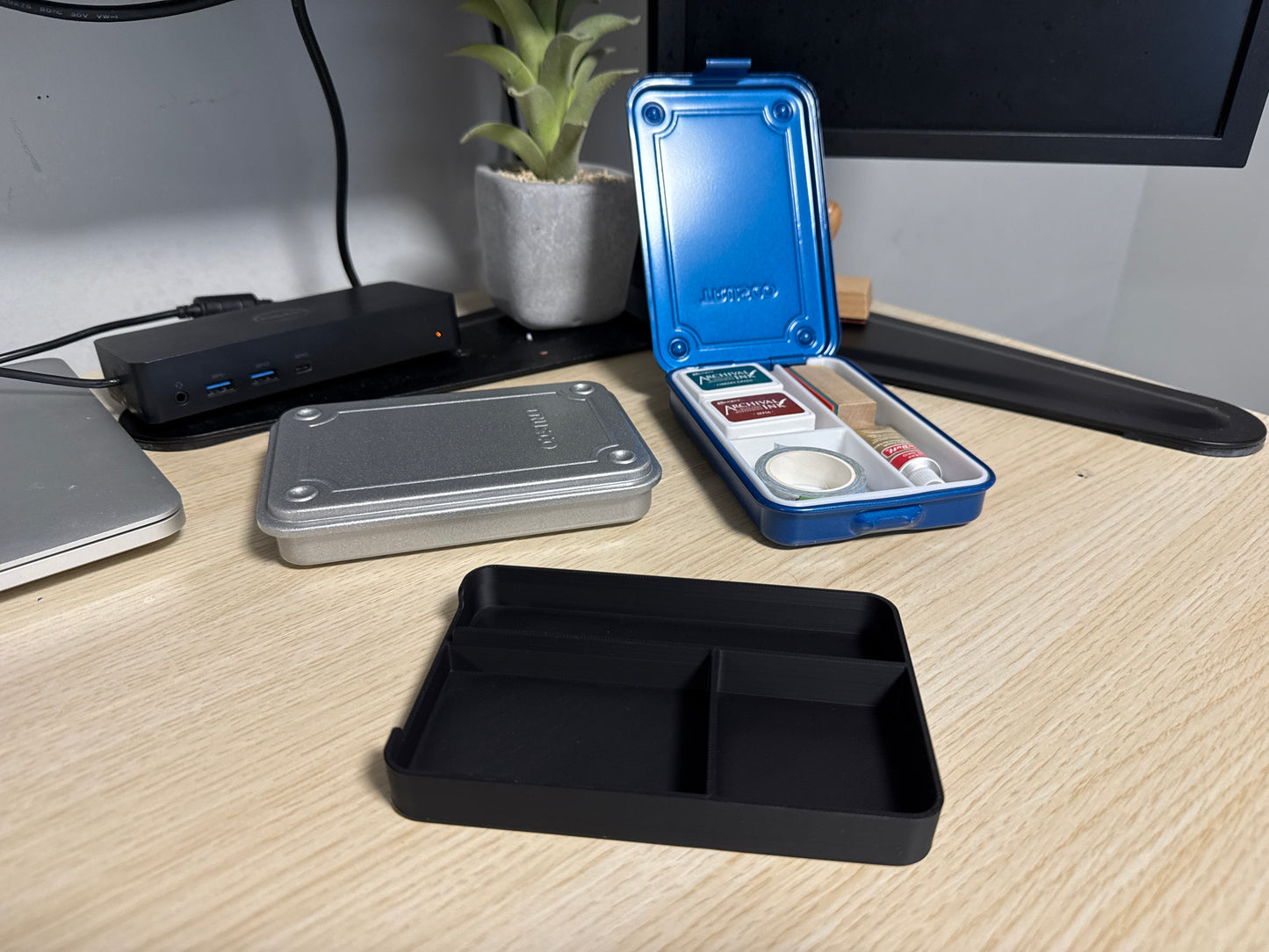 A set of 3D printed black inserts of various sizes displayed on a desk next to a blue trusco toolbox, and a silver trusco toolbox.
