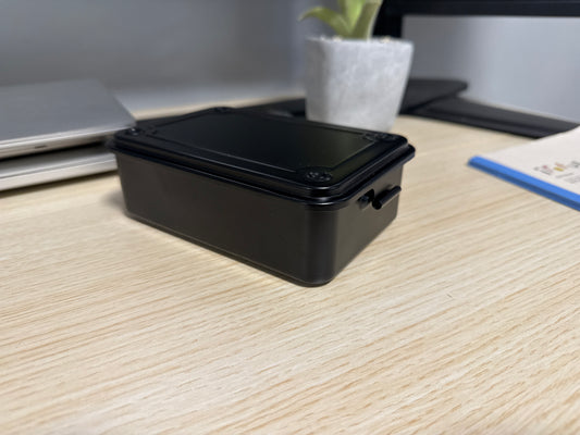 A black Toyo T-150 stackable tool box placed on a wooden surface, with a laptop, plant, and other items in the background.