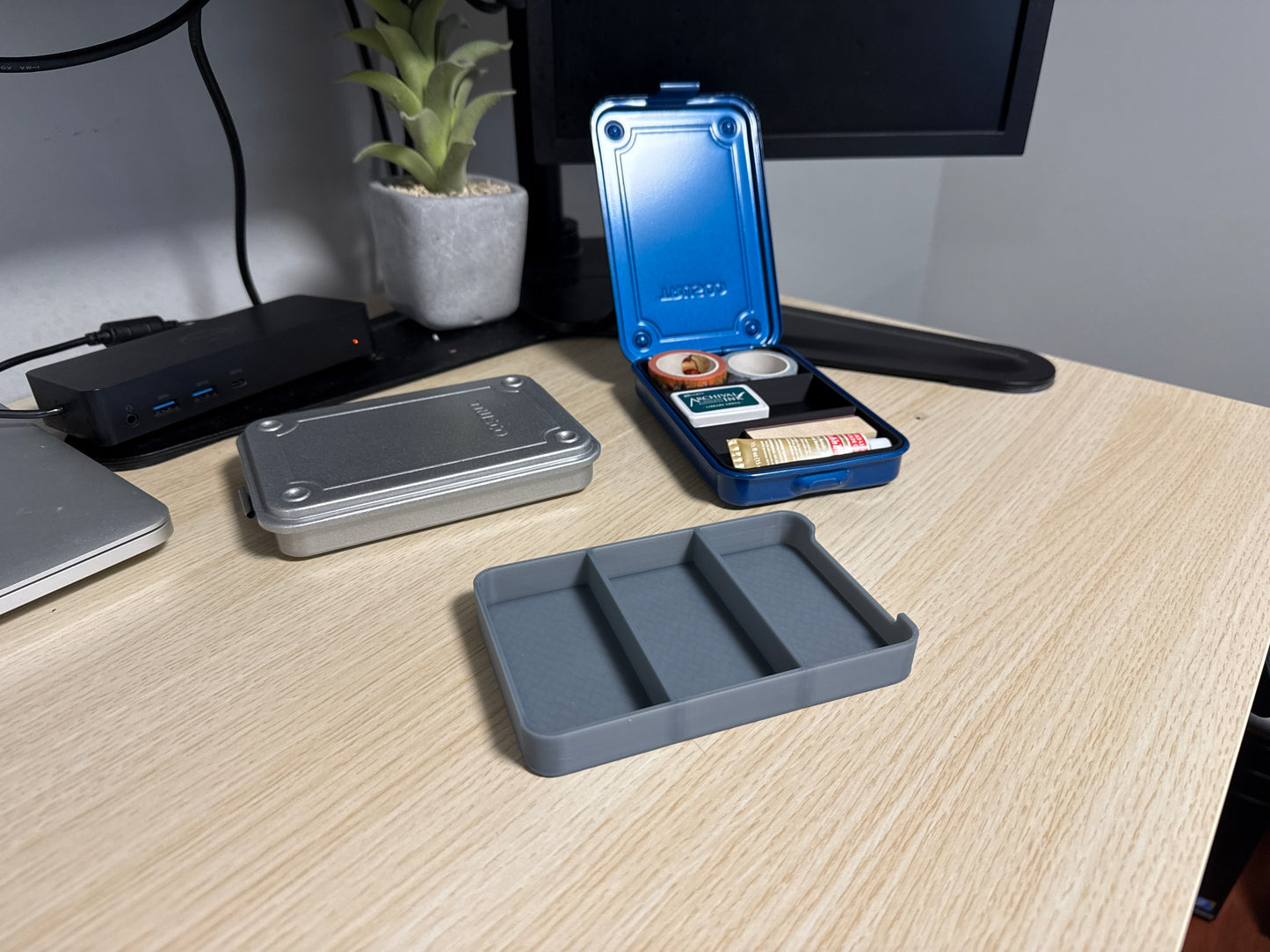A set of 3D printed gray inserts of various sizes displayed on a desk next to a blue trusco toolbox, and a silver trusco toolbox.